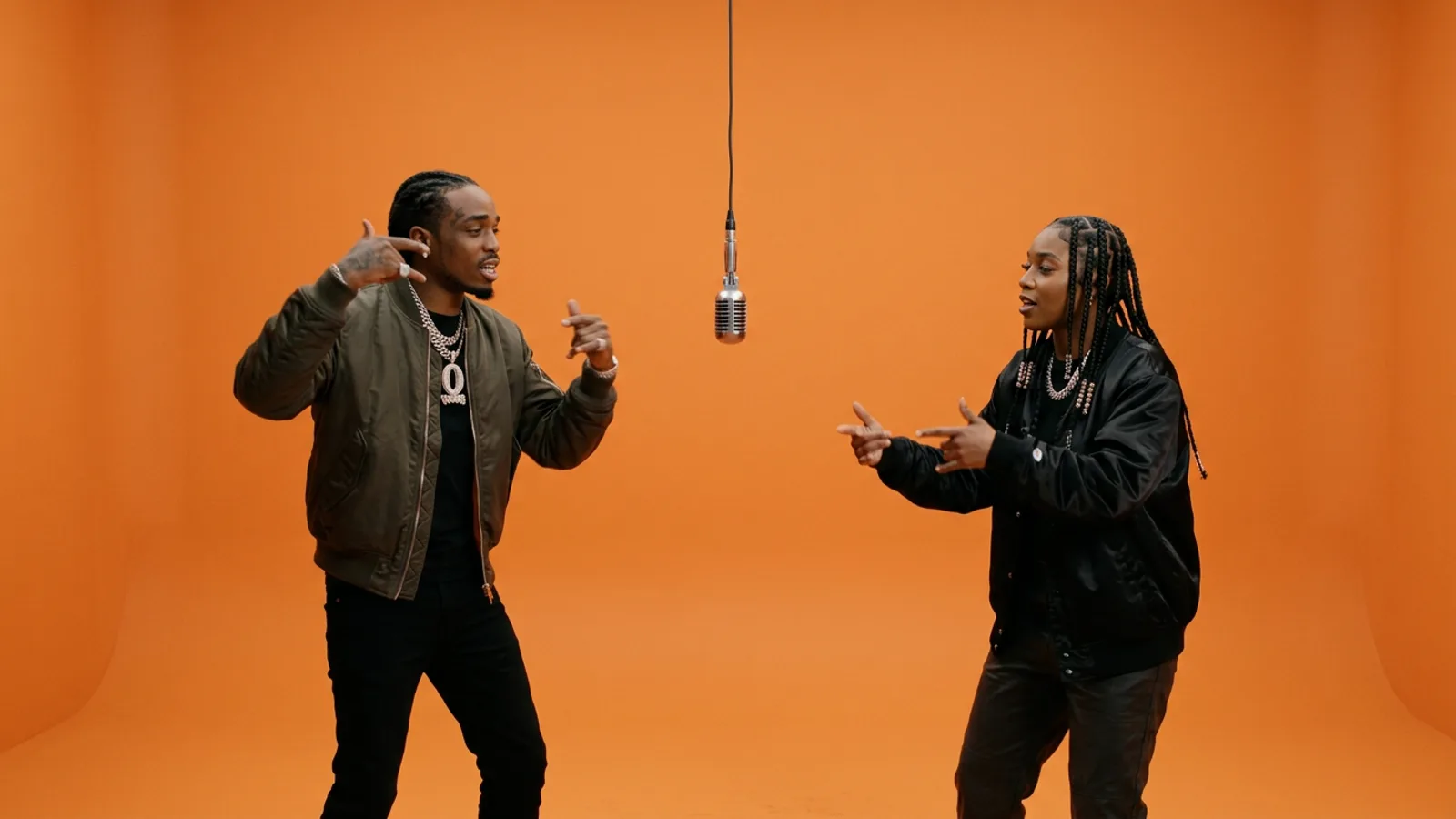Two streetwear performers rapping beside a suspended microphone in an orange studio